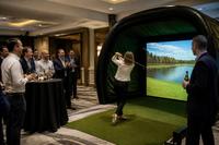 A colleague takes a swing in the simulator at a work event while the team watches