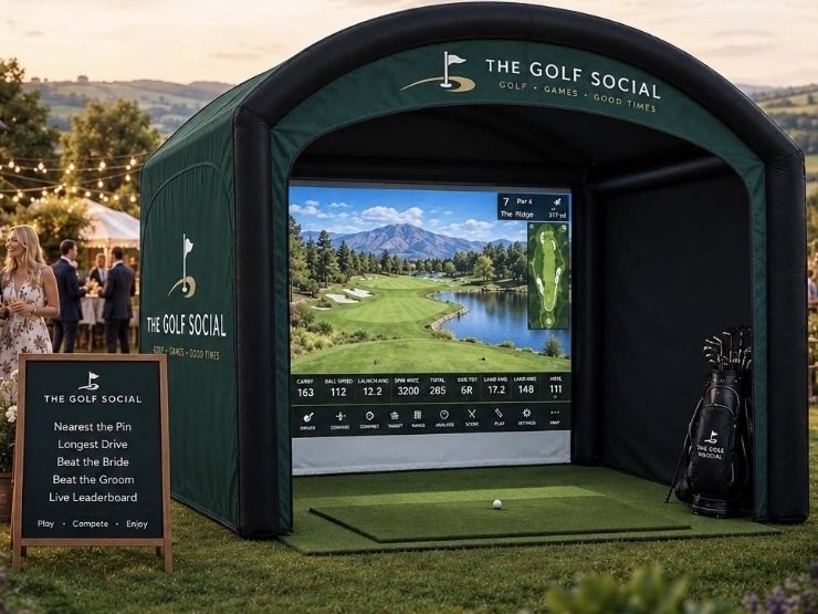 The Golf Social inflatable simulator set up on a lawn, with a games board beside it listing nearest the pin and longest drive